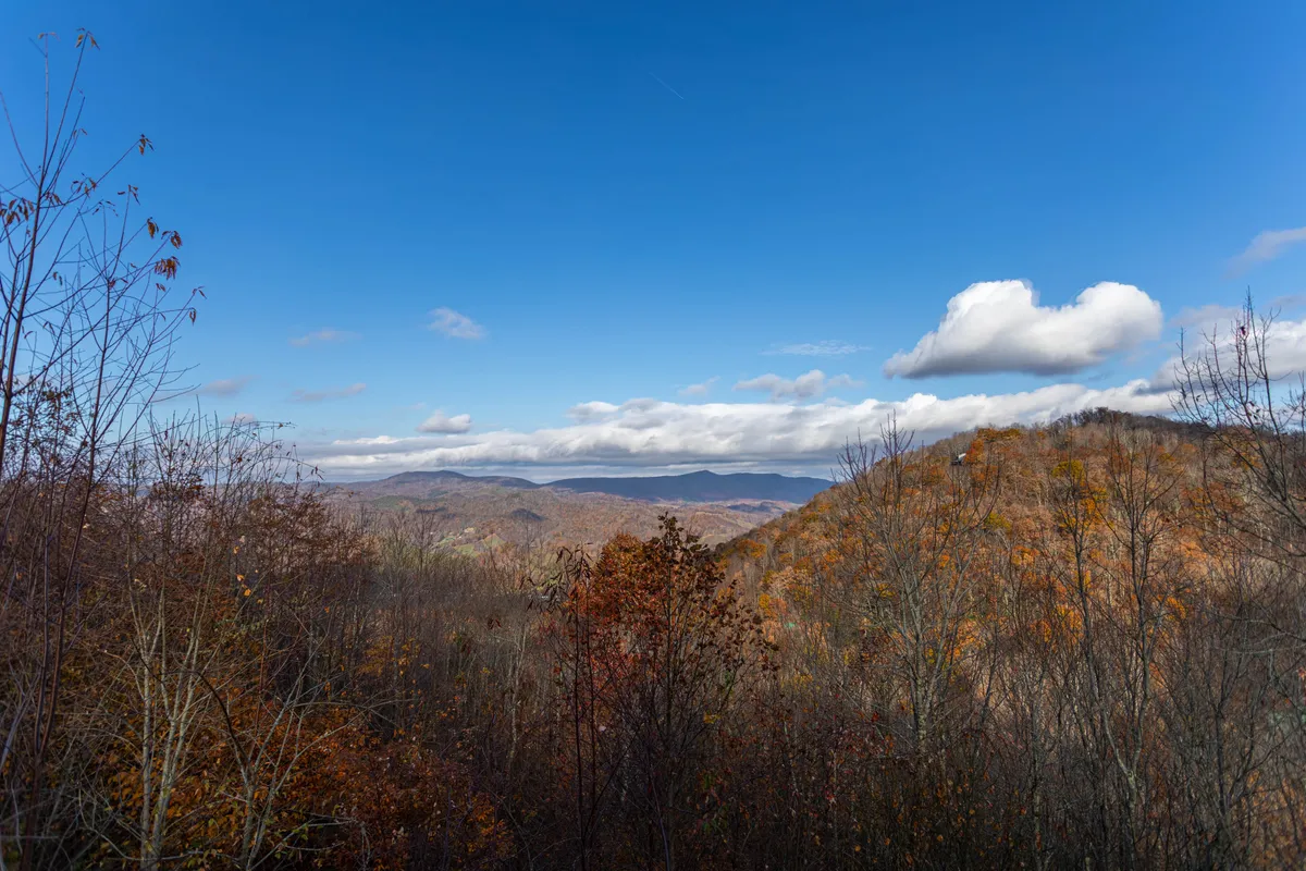 A breathtaking panoramic view of the Blue Ridge Mountains adorned with autumn foliage, under a sky dotted with soft clouds. The scene captures the tranquil beauty of the region, with opportunities for hiking, wildlife observation, and romantic picnics against a stunning mountainous backdrop.