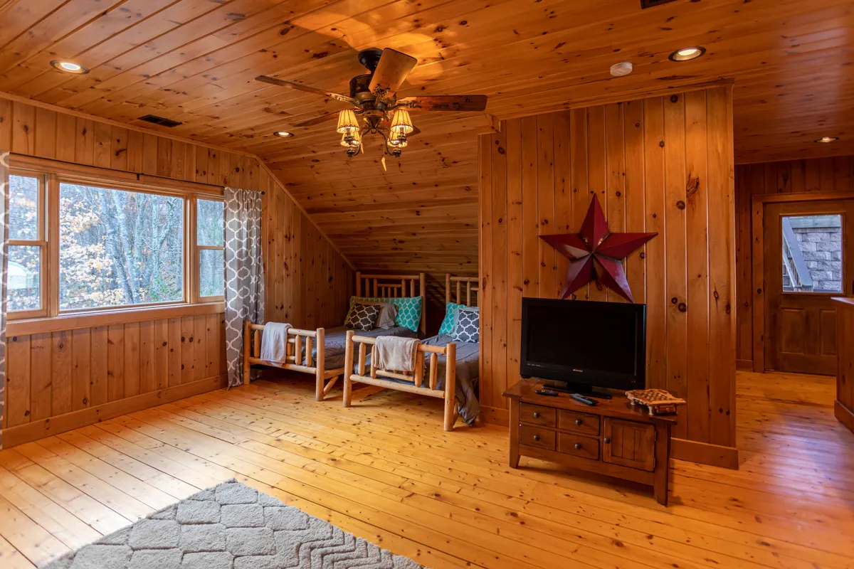 A rustic living area featuring wooden paneling, a large window with scenic views, comfortable furniture, and homey decorative touches. The scene feels perfect for watching sunsets, playing board games, or enjoying casual family conversations, with the outdoors always visible as a backdrop.