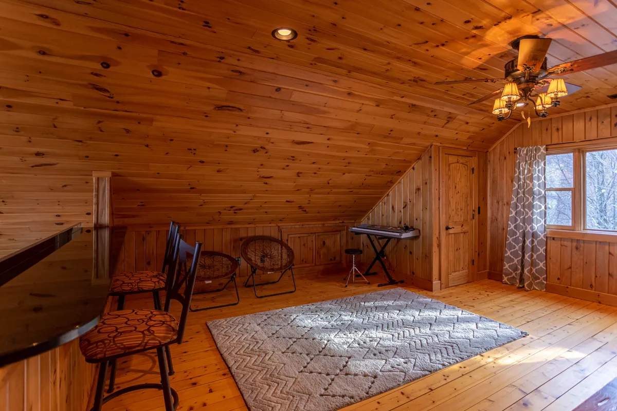 A view of a cozy nook with wooden walls, a bar area, musical keyboard, rug, and a bright window. The setting is perfect for socializing, music sessions, or enjoying coffee while looking outside.