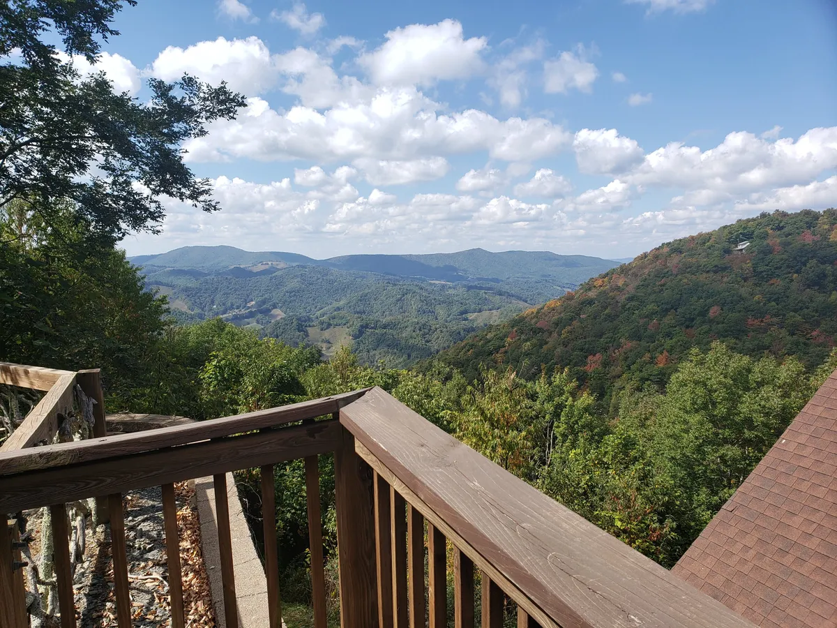 A serene mountainous landscape is visible beyond a rustic wooden railing, with misty clouds rolling over the peaks. The view suggests a vantage point ideal for stargazing or enjoying a quiet moment, echoing the quiet intimacy of the retreat.